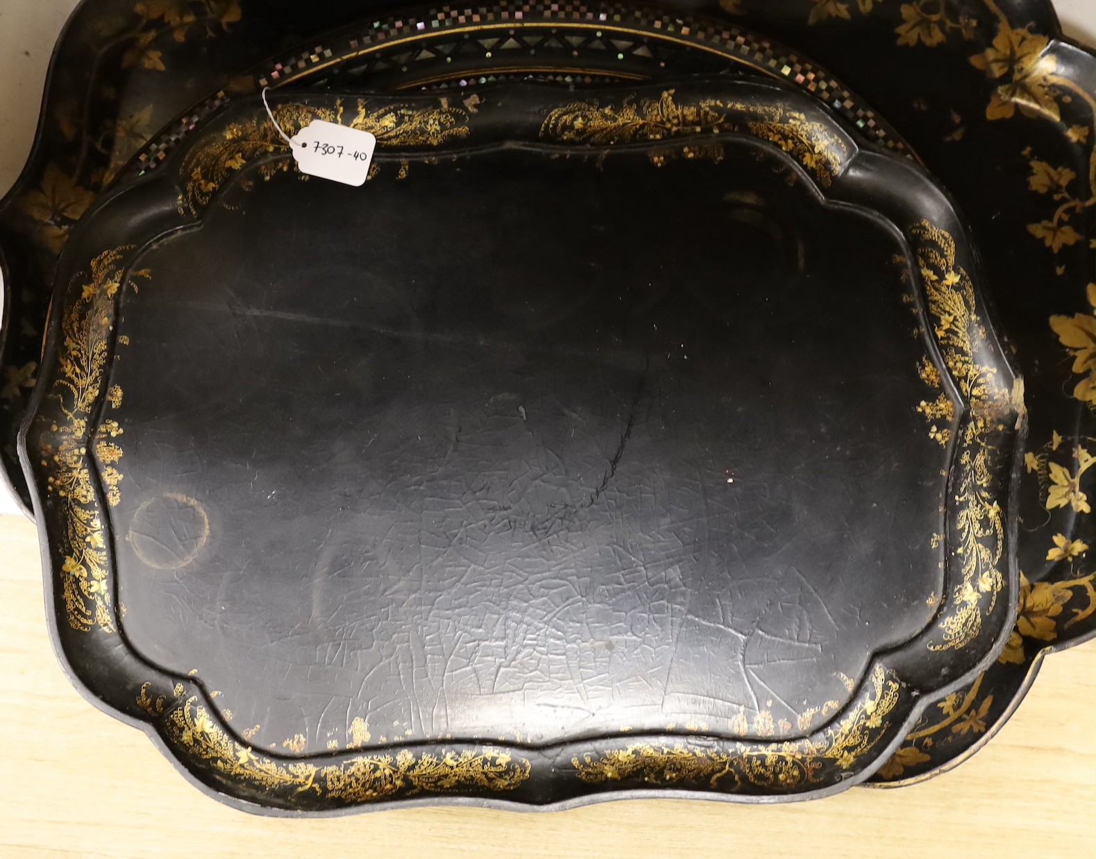 Four papier-mâché-mâché trays, a roundel and bowl, largest tray 80cms wide